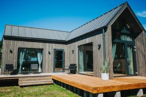 a wooden house with a deck and glass doors at Goba Sauleskempings in Mērsrags