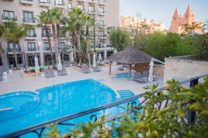 a swimming pool with chairs and an umbrella next to a building at Maritim Antonine Hotel & Spa in Mellieħa