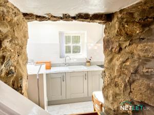 une cuisine avec des armoires blanches et un évier dans un mur en pierre dans l'établissement Hafan Hedd - Romantic Rural Retreat in Pembrokeshire, à Solva 43 autres photos