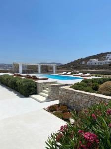 a swimming pool with a stone wall and flowers at Villa Conza Mykonos in Agios Ioannis Mykonos
