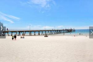 a beach with a pier and people on the sand at Pier 108 Glenelg in Glenelg