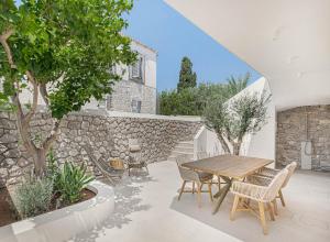 un patio con mesa de madera, sillas y pared de piedra. en Pearl House - Luxurious new beach villa in Spetses stunning view en Spétses