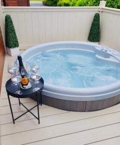 a jacuzzi tub with a table with wine glasses and a bottle at Green Acres Retreat Lodge with Hot Tub in Malton