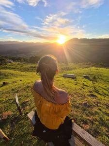 a woman sitting on a fence watching the sunset at Ap. Shalom. Pousada Colina dos Ventos in Urubici