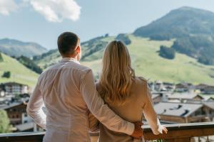 mężczyzna i kobieta stojący na balkonie z widokiem na góry w obiekcie Hotel Alpine Palace w Saalbach Hinterglemm