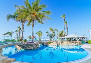 a pool at a resort with palm trees and a bridge at Leonardo Cypria Bay in Paphos