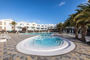a swimming pool with palm trees and buildings at Apartamentos LIVVO Morromar in Puerto del Carmen