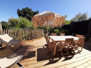 una terraza de madera con mesa, sillas y sombrilla de paja en Le Cottage du Bois Flotté en Saint-Malo