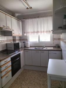 een keuken met witte kasten, een wastafel en een raam bij Primera linea de Playa a 1km del puerto de Denia in Denia