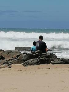 a man and a child sitting on rocks on the beach at Laughing Gecko Lodge2 in Southbroom