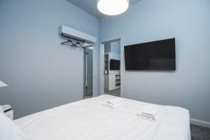 a bedroom with a white bed and a flat screen tv at Roze Park Rooms in Liepāja
