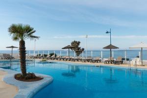 a swimming pool with chairs and umbrellas on the beach at AluaSun Far Menorca in S'Algar