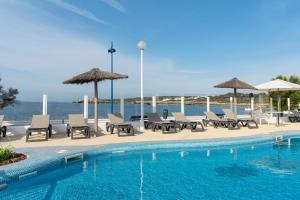 una piscina con sillas y sombrillas junto al océano en AluaSun Far Menorca, en S'Algar