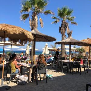 people sitting at tables on the beach with umbrellas at Eco-responsible stay on the historical sailing boat of the Gaiarta Project - come and stay with our crew and get the whole boat experience in Saint-Cyprien