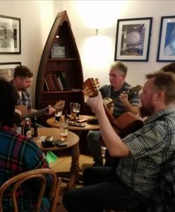 un grupo de personas sentadas alrededor de una mesa tocando la guitarra en Glenuig Inn en Lochailort