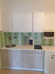 eine Küche mit weißen Schränken, einer Spüle und einer Mikrowelle in der Unterkunft Apartments Vidakovic in Ugljan
