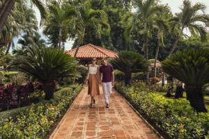a man and a woman walking down a path in a garden at El Embajador, a Royal Hideaway Hotel in Santo Domingo