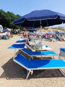 rząd niebieskich krzeseł i parasol na plaży w obiekcie Stella Mare w mieście Santa Flavia