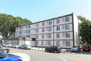 a large white building with cars parked in a parking lot at Hotel Proton K3 in Neptun