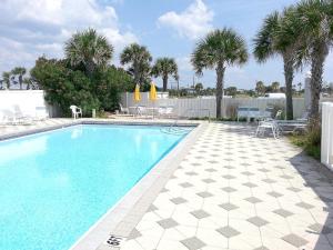 a swimming pool with chairs and umbrellas and palm trees at Island Sands 206 in Fort Walton Beach