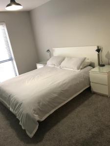 een slaapkamer met een wit bed, een nachtkastje en een raam bij Fabulous Portstewart Modern Seaside House NITB in Portstewart