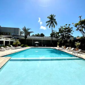 a large blue swimming pool with chairs and palm trees at Delphin Beach Hotel in Guarujá