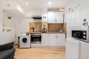ロンドンにあるBeautiful Hyde Park Studio Flatのキッチン(白いキャビネット、洗濯機、乾燥機付)