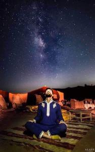 Ein Mann sitzt in Meditation unter den Sternen in der Unterkunft Bivouac ZAGORA in Zagora