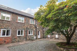 una vieja casa de piedra con un árbol delante en Maple Cottage, en Keswick