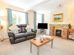 a living room with a leather couch and a fireplace at Maple Cottage in Keswick