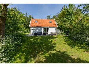 een klein wit huis met een oranje dak in een tuin bij Holiday home in the middle of the wooded dune landscape close to the beach in Dishoek