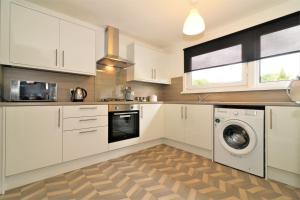 a kitchen with white cabinets and a washer and dryer at Signature - Troon View in East Kilbride