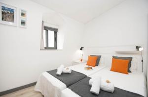 a white bedroom with a large white bed with orange pillows at In Downtown - Villa Serenity in Albufeira