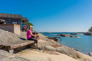 une femme assise sur un banc à côté de l'eau dans l'établissement Isakssons Cottage 4, à Föglö