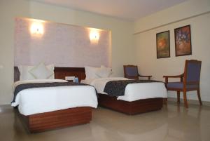 two beds in a hotel room with two chairs at Hotel Abigail Regency in Shirdi