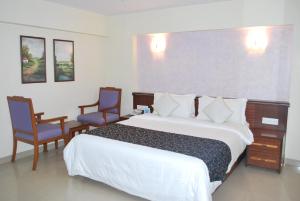 a bedroom with a large bed and two chairs at Hotel Abigail Regency in Shirdi