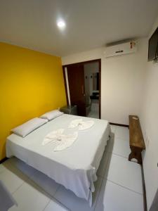 a white bed in a room with a yellow wall at Piratas do Morro Pousada in Morro de São Paulo