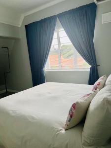 a white bed with blue curtains and a window at Bella Lux Villa in Durban