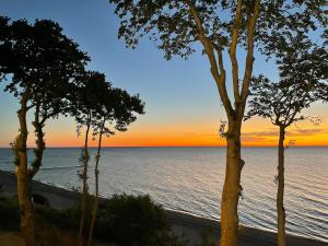 una puesta de sol sobre el océano con árboles en el primer plano en APARTAMENT 36 na klifie z widokiem na morze ADULTS ONLY, en Rewal