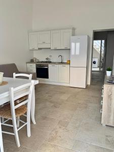 a white kitchen with a table and a refrigerator at Le Margherite Holiday Home - Campomarino di Maruggio, zona Acquadolce Cirenaica in Maruggio