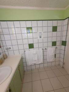 La salle de bains est pourvue de carrelage blanc, d'un lavabo et de serviettes. dans l'établissement Burns' Apartment, à Cap Estate