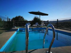 a blue swimming pool with an umbrella and chairs at Alcázar Milmanda in Milmanda