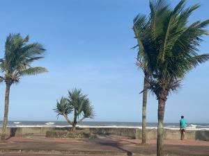 Un hombre parado entre dos palmeras cerca del océano. en Casa de praia aconchegante próxima ao centro, en Mongaguá