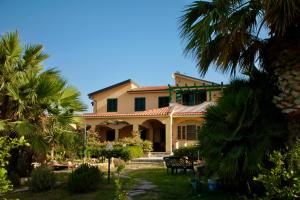 a large yellow house with palm trees in the yard at Hostel Vela Vega in Butera