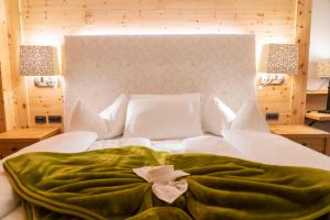 a white bed with a green blanket on top of it at Hotel Cesa Tyrol in Canazei