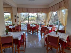 un restaurante con mesas blancas, sillas rojas y ventanas en Phaethon Hotel en Cos