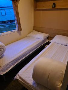 two beds in a small room with a window at Cosy, family caravan near the beach in Clacton-on-Sea
