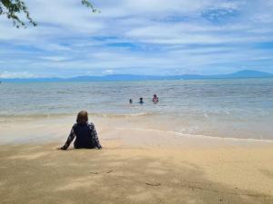 Eine Frau, die am Strand sitzt und Menschen im Wasser beobachtet. in der Unterkunft Calatagan's Bahay Kubo - with Beach Access in Batangas City