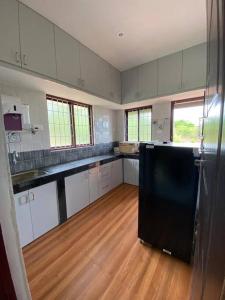 uma grande cozinha com armários brancos e um frigorífico preto em AR Springfields(1), amidst lush green scenic view em Manipal