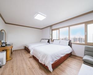 a bedroom with two beds and a couch and windows at Top Island Hotel in Jeju